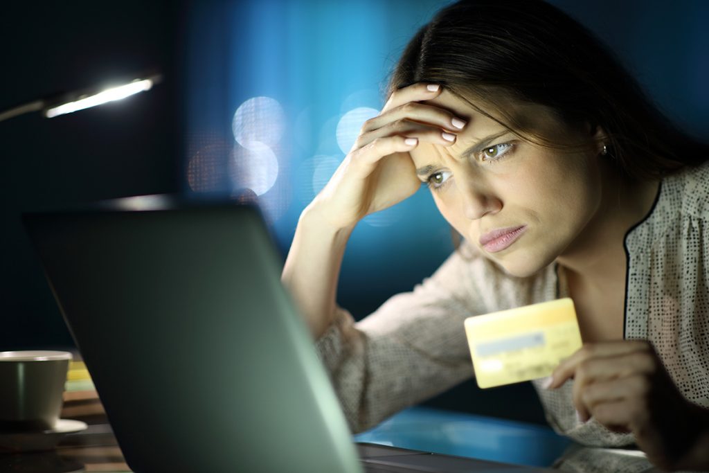 Une femme regarde un écran d'ordinateur tout en tenant une carte de crédit.