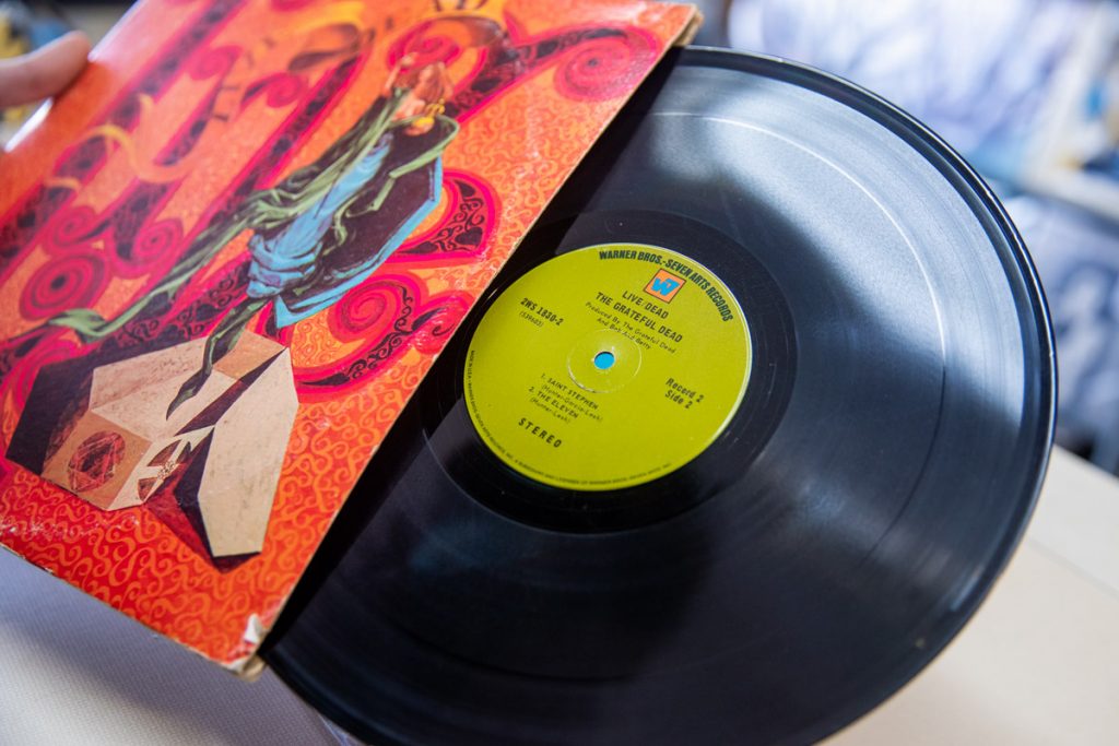 Une personne sort l'album de son live / mort de Grateful Dead de sa manche de couverture qui est orange et rose. Le record se vend 40 €.