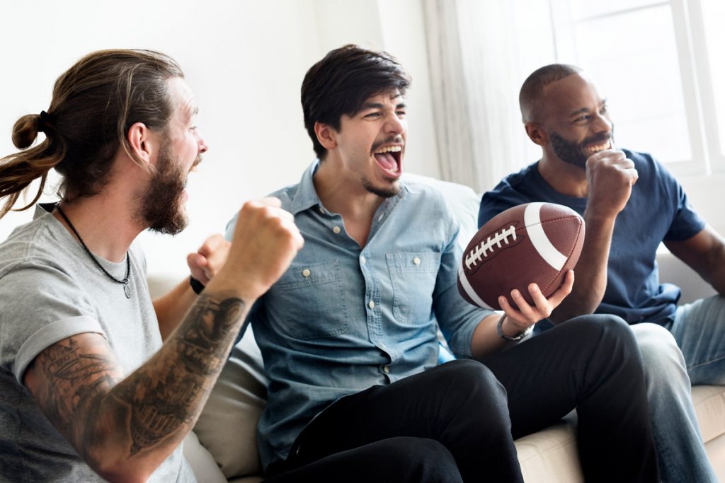 Trois hommes réagissent de manière positive à la télévision tout en regardant un match de football.