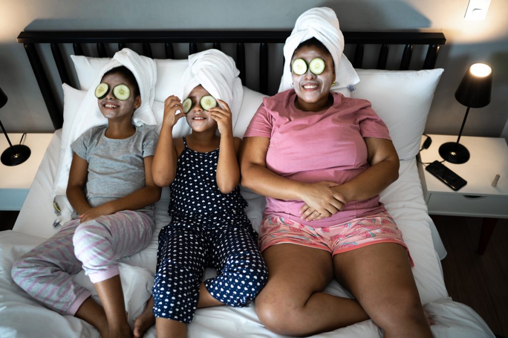 Une mère et ses deux filles se sont allongées au lit avec des masques du visage et des concombres sur leurs yeux.