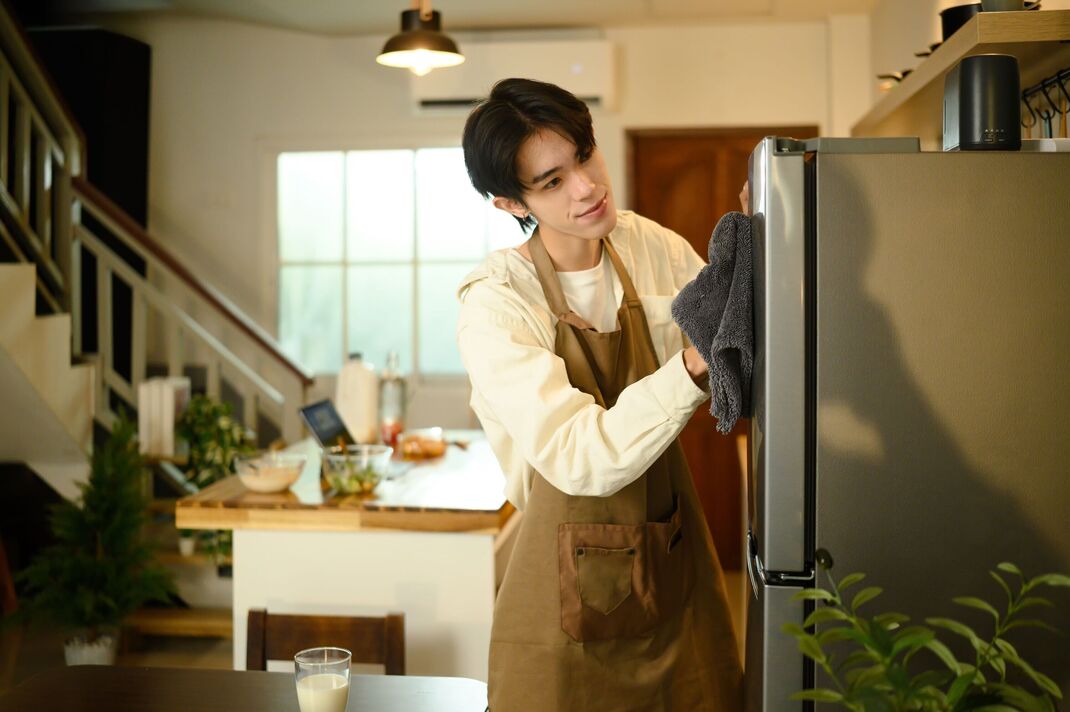 Homme souriant faisant des tâches ménagères, nettoyant le réfrigérateur avec un tissu