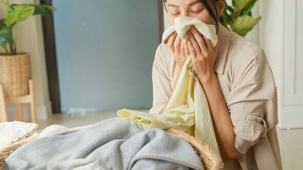 Gros plan de la belle jeune femme asiatique sentant des vêtements propres et souriant tout en faisant la lessive à la maison. Activité de la vie quotidienne 