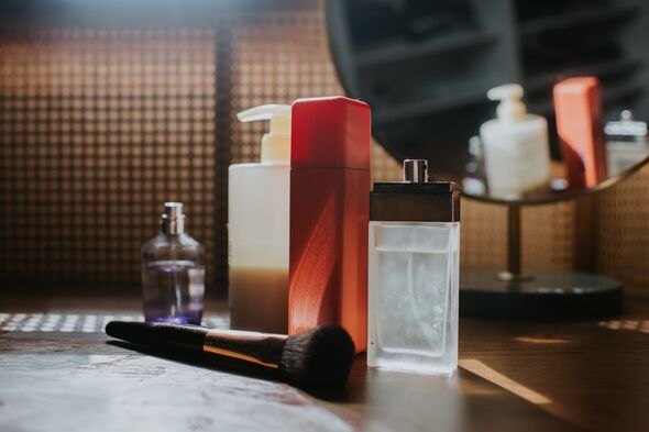 Divers produits de beauté, y compris le parfum, sur une coiffeuse devant un miroir de vanité