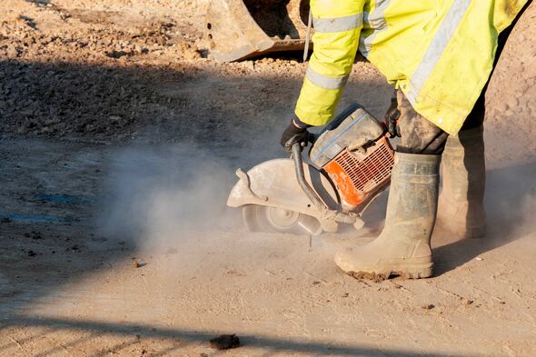 Un individu, vêtu d'une tenue de protection comprenant une veste et des bottes haute visibilité, est en train d'utiliser un outil électrique. 