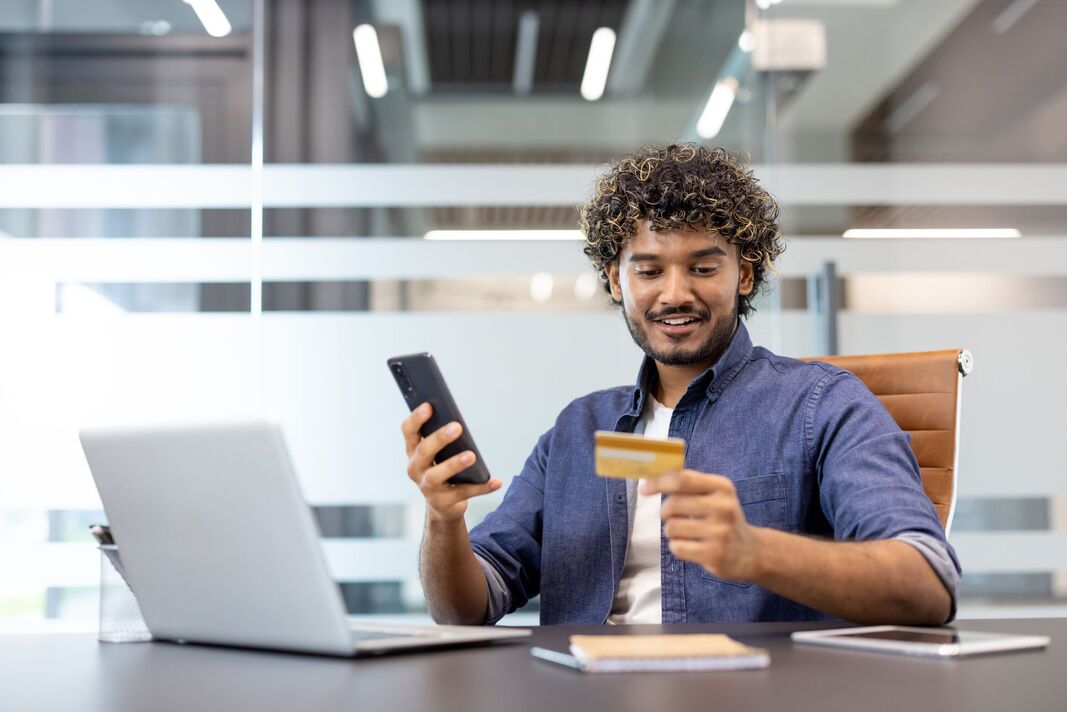 homme assis au bureau, utilisant un téléphone portable et une carte de crédit