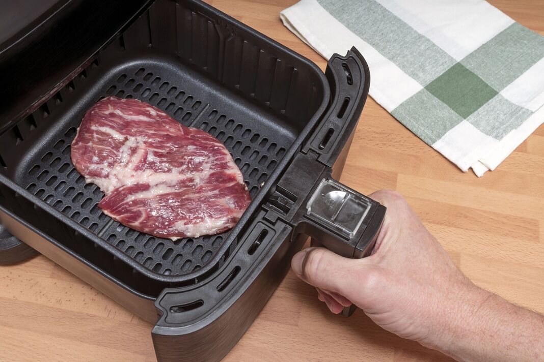 CUISSON À LA MAIN D'UN STEAK DE VIANDE ROUGE CRU DANS UNE FRITEUSE À AIR DANS LA CUISINE. VUE DE DESSUS.