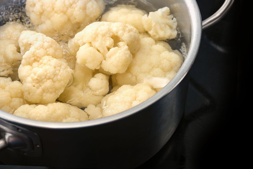 Chou-fleur dans de l'eau bouillante dans une casserole en acier inoxydable sur une table de cuisson noire, cuisson de légumes sains, espace de copie, mise au point sélectionnée