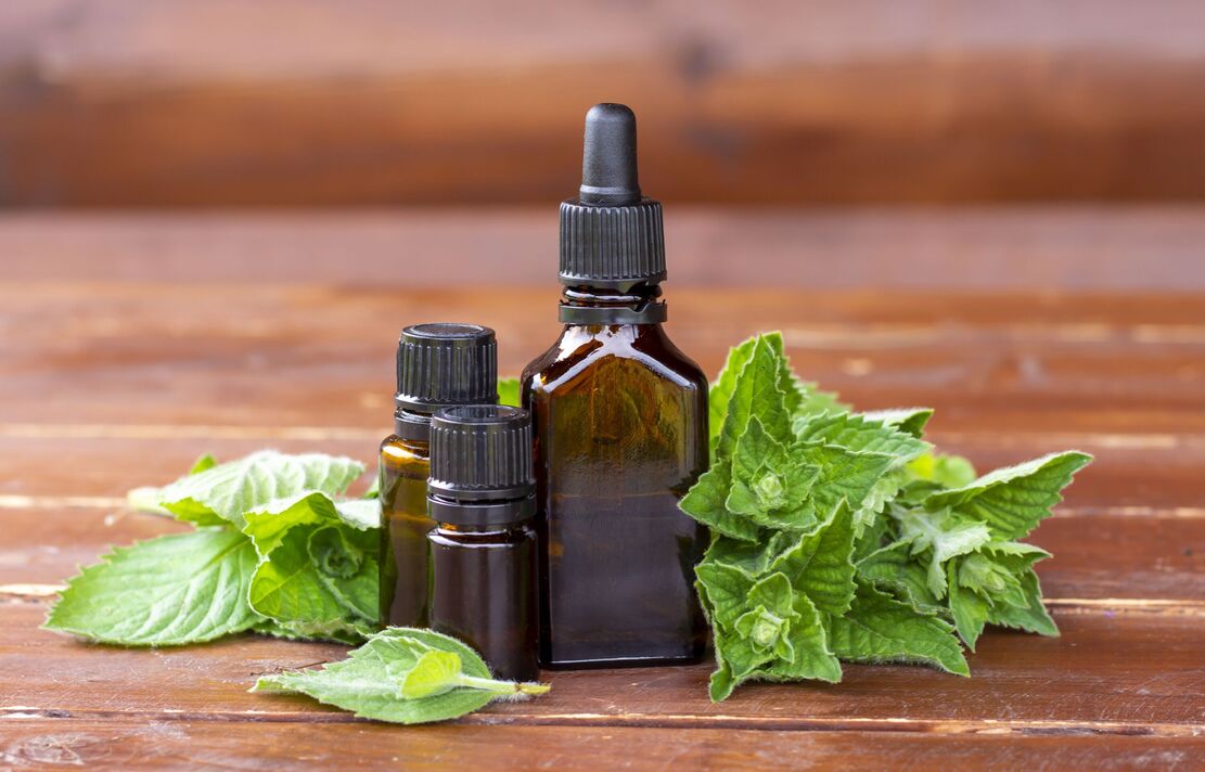 Huile essentielle de menthe poivrée. Une bouteille en verre foncé (marron) avec de l'huile essentielle de menthe et de la menthe fraîche sur une table en bois