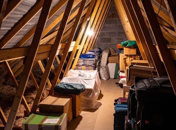 Un grenier caractérisé par des poutres en bois et un plafond mansardé. Diverses boîtes et objets de rangement sont placés au sol, avec