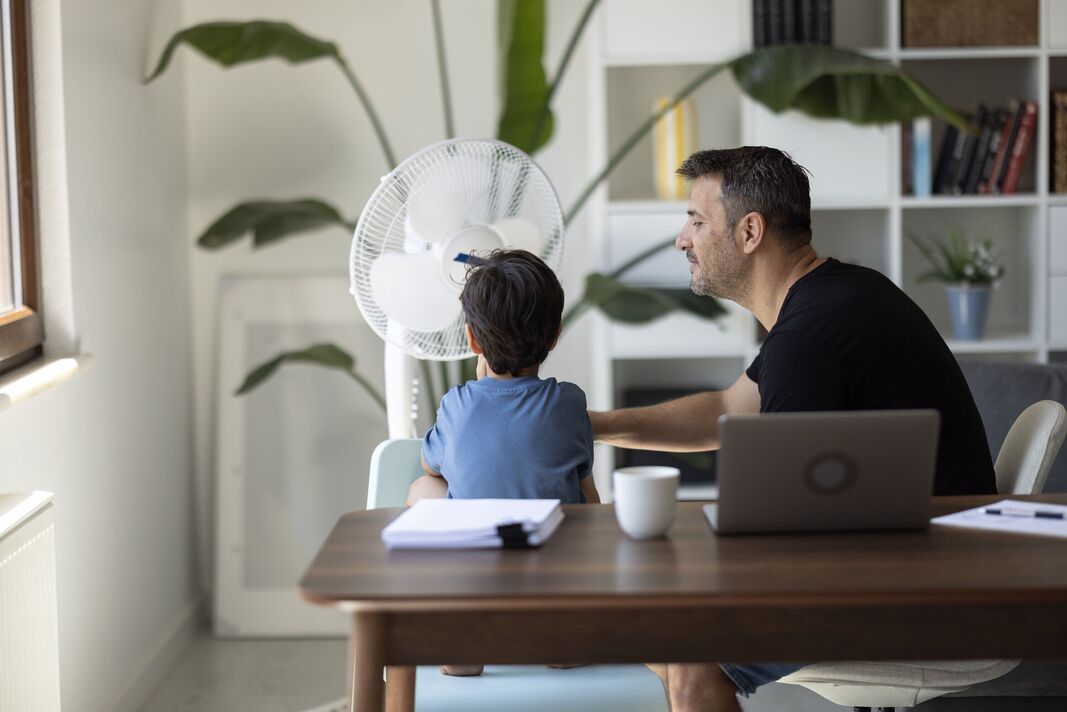 Père et fils se rafraîchissent avec un ventilateur au sol à la maison, restant à l'aise pendant la canicule estivale