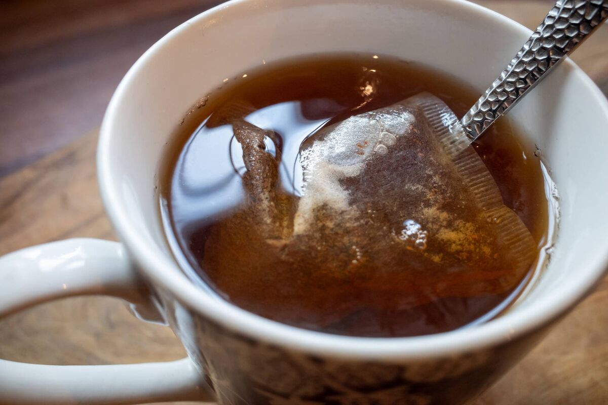 Une tasse à café blanche avec un liquide brun et un glaçon sur une surface en bois. Le liquide a une couleur riche et sombre et semble être Une tasse à café blanche avec un liquide brun et un glaçon sur une surface en bois. Le liquide a une couleur riche et sombre et semble être