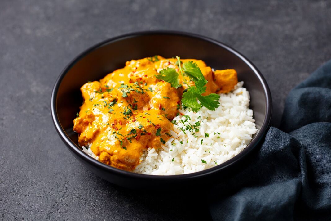 Curry de poulet crémeux sur riz blanc moelleux, garni de coriandre fraîche. Fond gris. Gros plan.