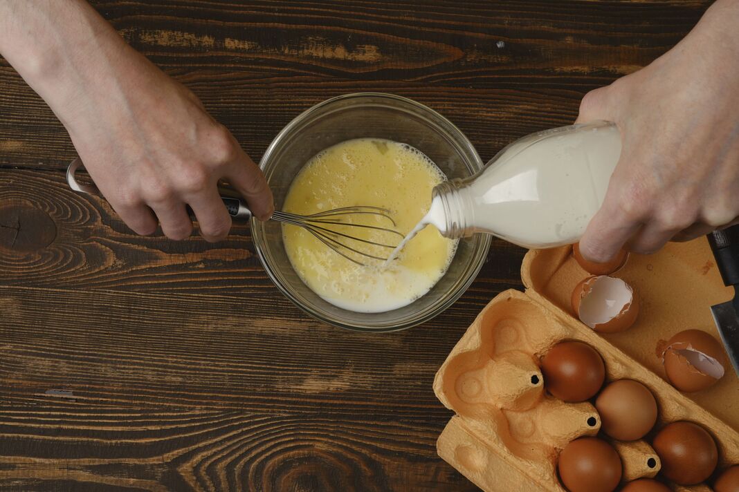 Vue de dessus de verser du lait dans les œufs. Préparation d'une omelette