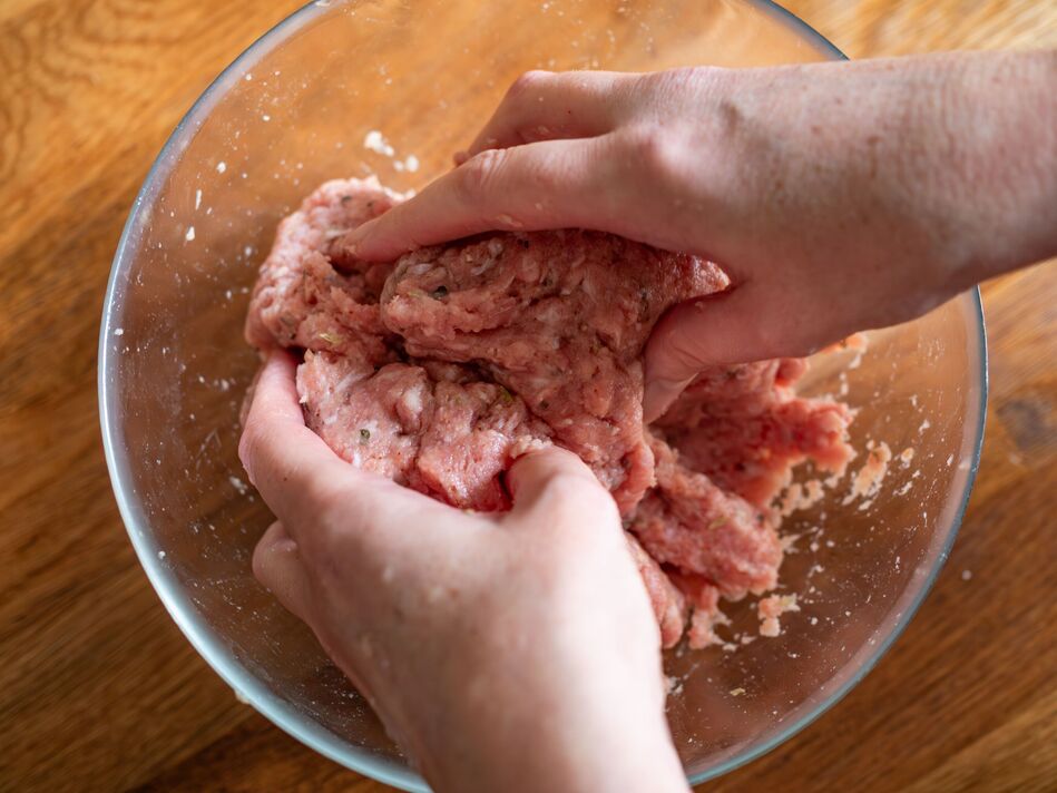 Préparation de viande de porc hachée crue dans un bol en verre, gros plan des mains