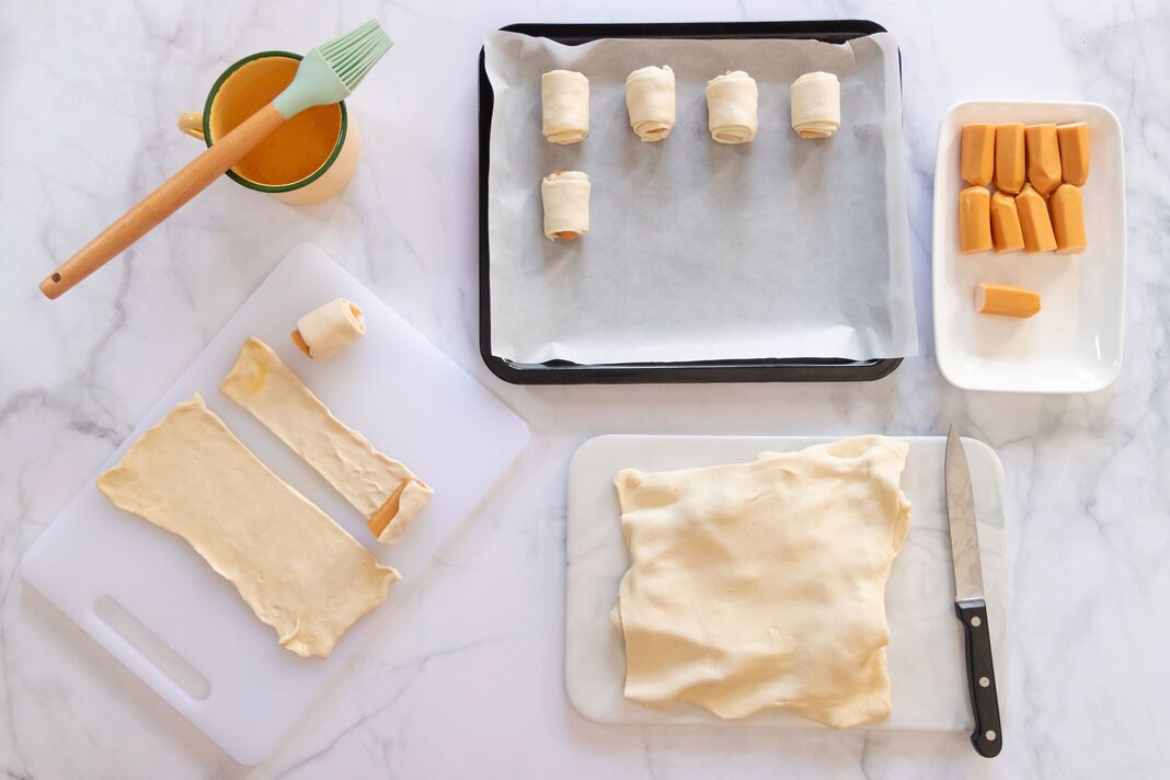 Ingrédients de cuisson pour mini saucisses enveloppées dans une pâte feuilletée avec des ustensiles de cuisine sur une table en marbre blanc. Vue de dessus et espace de copie.