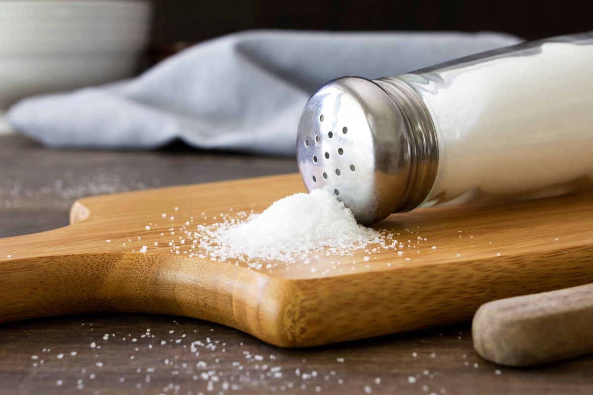 Un gros plan de sel s'échappant d'une salière sur une planche à découper en bois. Tourné sur une table de cuisine rustique en bois avec