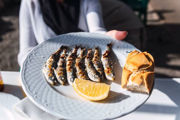 Une assiette blanche sur une table contient une sélection de poissons grillés accompagnés d'un quartier de citron et d'un morceau de pain. Une assiette blanche sur une table contient une sélection de poissons grillés accompagnés d'un quartier de citron et d'un morceau de pain.