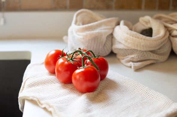 Bouquet de tomates sur vigne posées sur un sac de produits en coton en maille réutilisable sur un comptoir de cuisine moderne Bouquet de tomates sur vigne posées sur un sac de produits en coton en maille réutilisable sur un comptoir de cuisine moderne