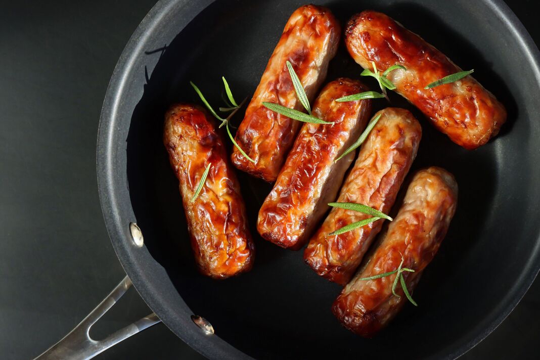 Image de six saucisses grasses frites dans une poêle, saucisses dorées assises dans une poêle antiadhésive, garniture d'herbes de feuilles de romarin, fond noir, vue élevée, espace de copie Image de six saucisses grasses frites dans une poêle, saucisses dorées assises dans une poêle antiadhésive, garniture d'herbes de feuilles de romarin, fond noir, vue élevée, espace de copie