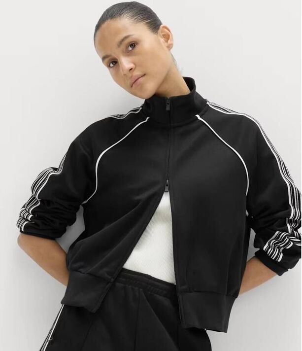 Un individu est représenté portant une veste noire et blanche avec un col haut et des rayures blanches distinctives le long des manches. T