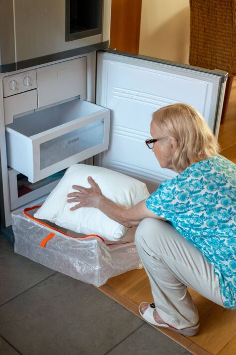 Femme âgée mettant un oreiller dans le réfrigérateur-congélateur. Comment rester au frais par temps chaud.