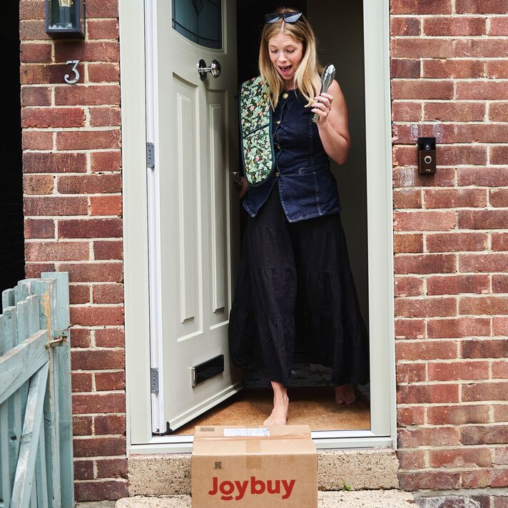 Une femme s'exclamant devant un colis Joybuy devant sa porte