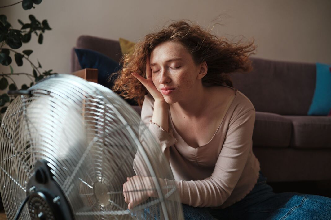 Femme insouciante se détendant près d'un ventilateur électrique à la maison, se rafraîchissant pendant la vague de chaleur à l'intérieur. Chaleur estivale