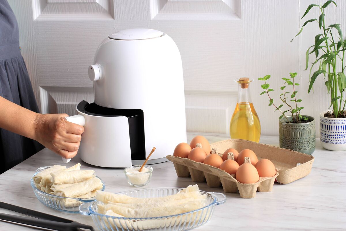 Plateau de friteuse à air ouvert à la main de femme. Une friteuse blanche ou une friteuse sans huile, des pinces, un plat de cuisson transparent et un plateau à œufs se trouvent sur le 
