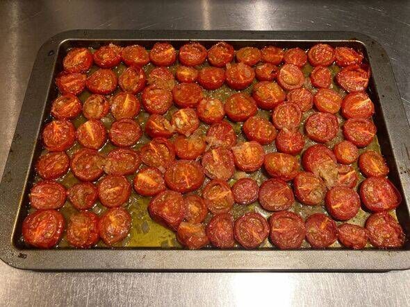 Tomates fraises cuites lentement coupées en deux, marinées dans l'huile d'olive, oignon haché et romarin sur une plaque à pâtisserie Tomates fraises cuites lentement coupées en deux, marinées dans l'huile d'olive, oignon haché et romarin sur une plaque à pâtisserie