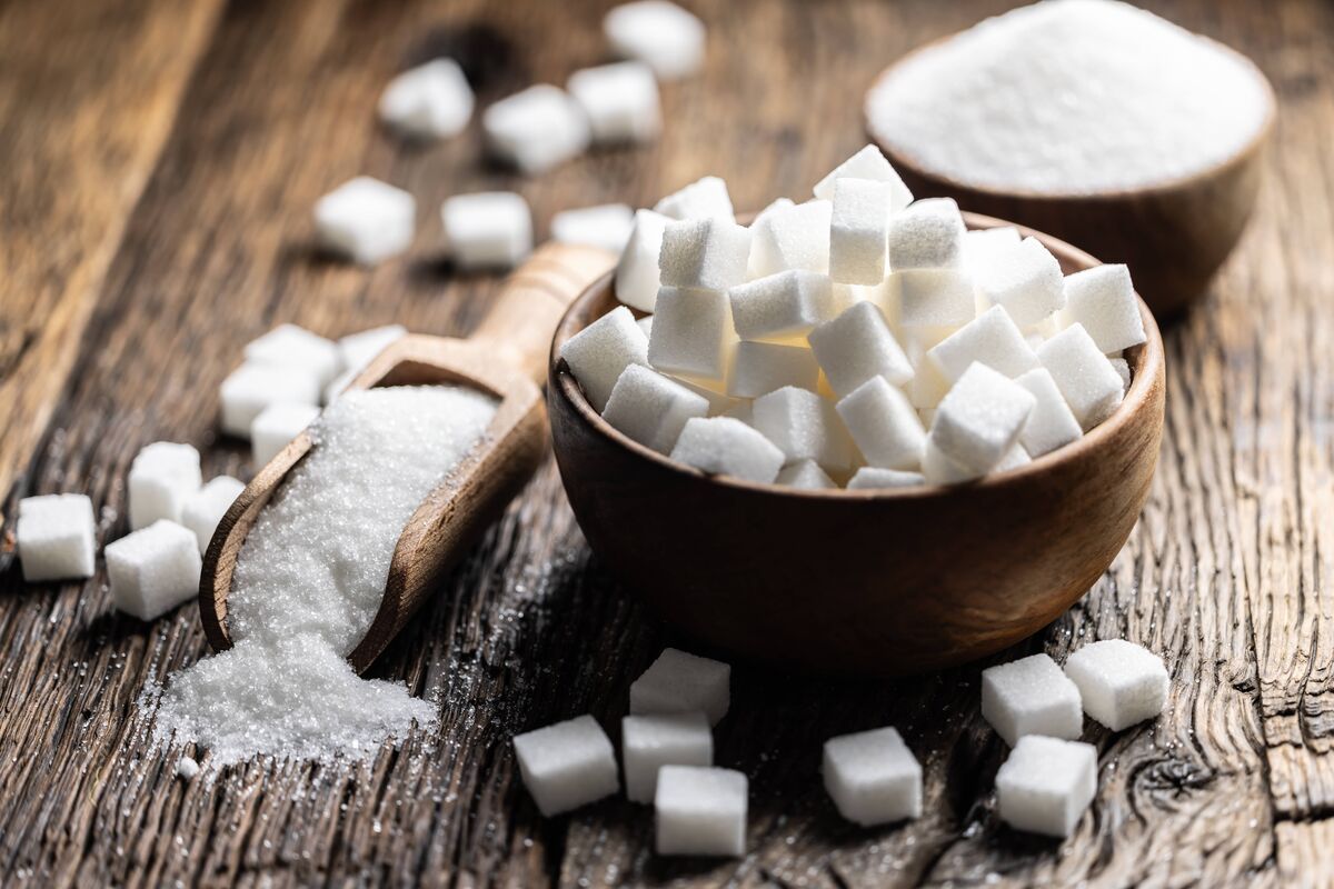 Sucre granulé dans une cuillère ou un bol en bois sur une vieille table en chêne.