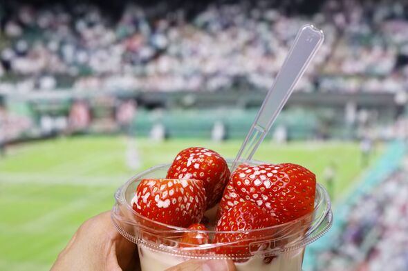 Image en gros plan d'une main tenant une tasse en plastique transparente remplie de fraises fraîches, avec un arrière-plan flou d'un sport Image en gros plan d'une main tenant une tasse en plastique transparente remplie de fraises fraîches, avec un arrière-plan flou d'un sport