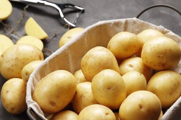Panier rempli de jeunes pommes de terre fraîches, d'une serviette et d'un couteau sur fond gris, vue du dessus